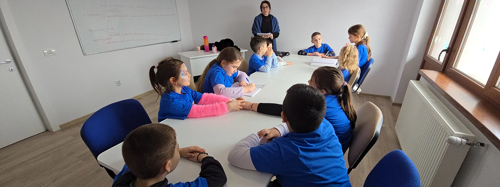 Copii rezolvând temele sub supravegherea profesorului